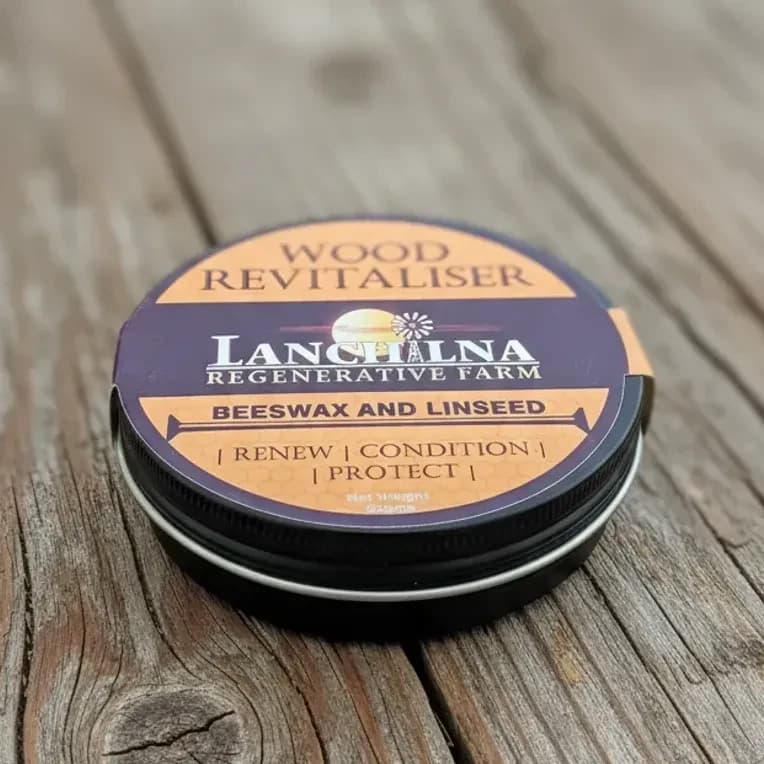 Tin of Beeswax Wood Revitaliser on a wooden surface. The label features the text "Languard Regenerative Farm" and "Beeswax and Linseed," with phrases "Renew," "Condition," and "Protect." The packaging is purple and orange.